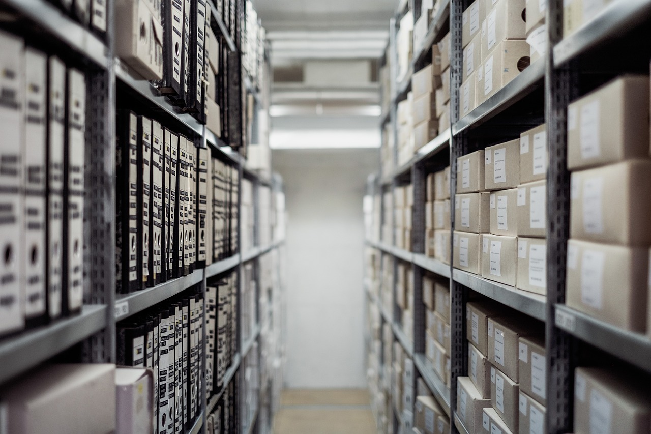Foto de um corredor de arquivo com estantes com caixas e pastas organizadas.