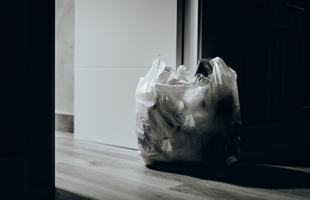 Foto de um saco plástico branco de lixo com papéis amassados dentro.