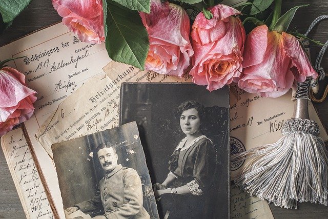 Foto contendo fotografias e papéis antigos, com escritos à mão, próximo de flores cor-de-rosa.